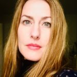 A white woman with blue eyes and blond hair framing her face looks directly at the camera.