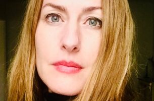 A white woman with blue eyes and blond hair framing her face looks directly at the camera.