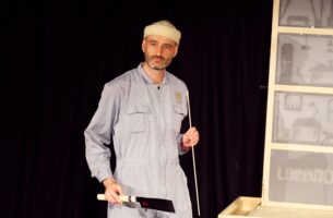 A man holds a butcher’s knife and long stick as he gazes at the audience.