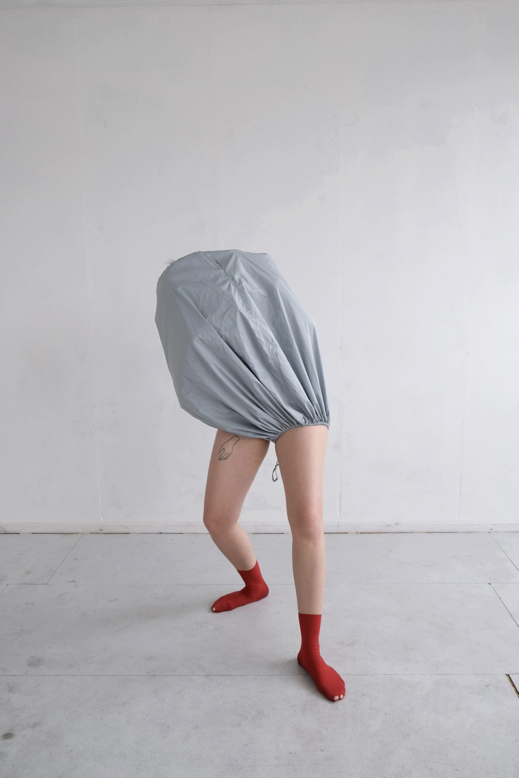 A person standing in an uneven stance with one leg far behind the other. The person is wearing a shirt that is pulled over their head and torso, and red socks with holes in them.