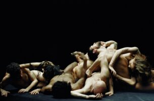 A tangle of seven dancers sprawls on the floor of a dark stage. Unclothed and in various states of recline, it is intimate, sensuous and raw.
