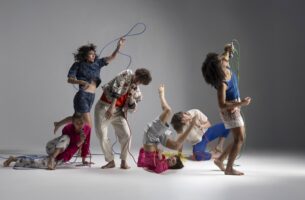 Image description: Six dancers are caught mid-action, each body making a different shape. They hold microphones with long colourful cords that hang and twist between them like squiggles on a page.