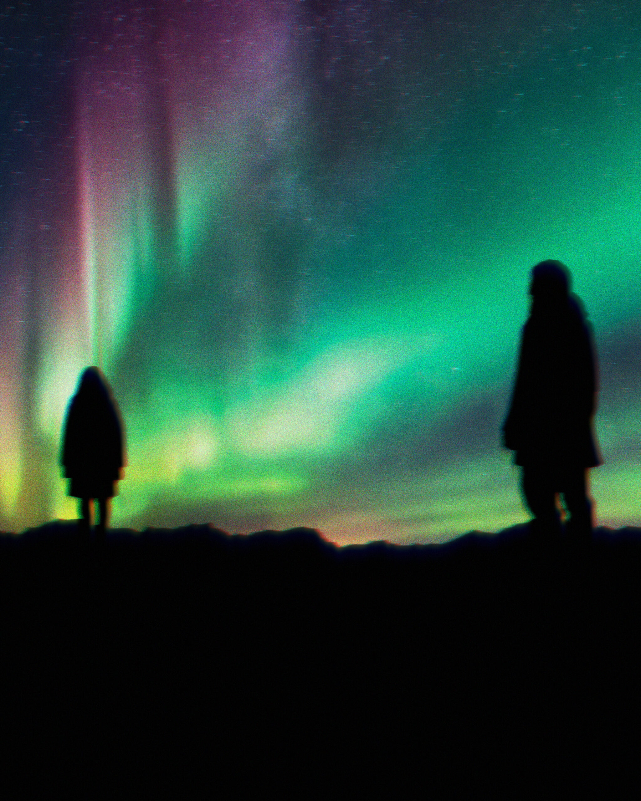 Image description: Two figures are silouetted on a ridge against the bright background of the northern lights, which fills the sky with glowing greens and pinks.